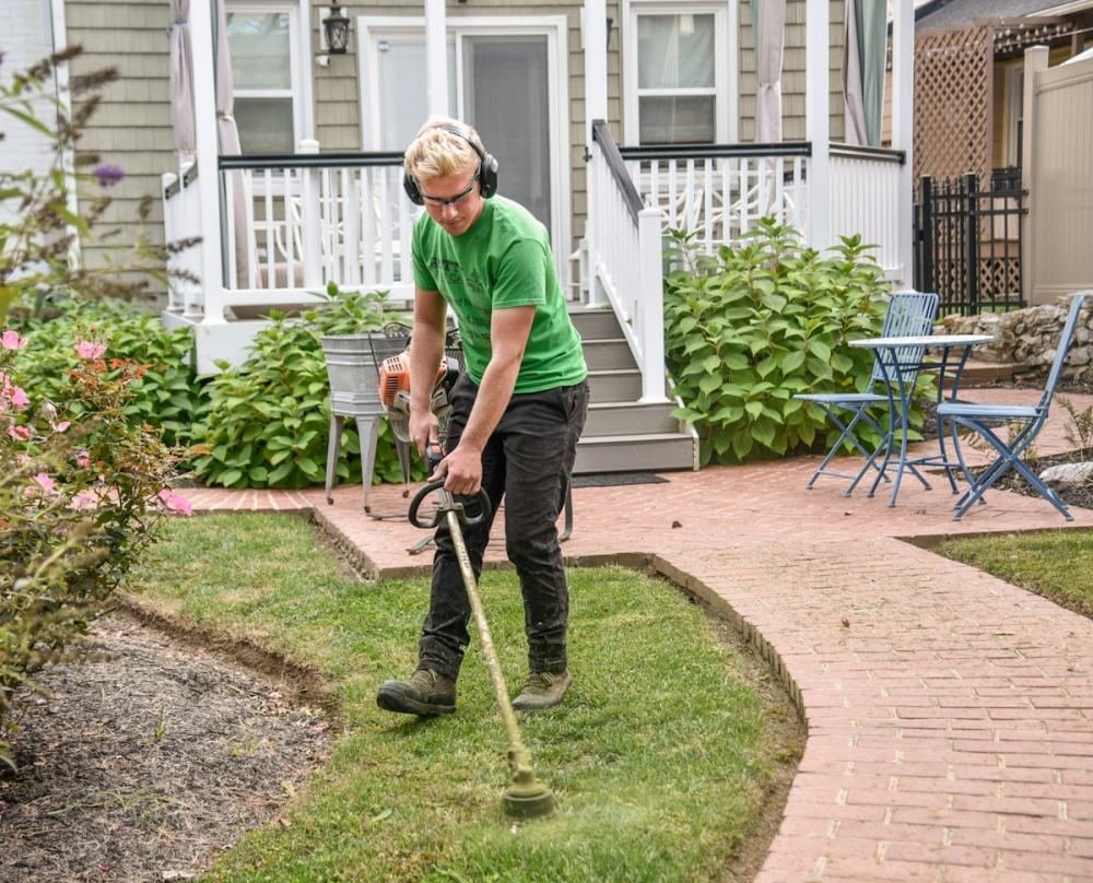 A landscaper edging a bed beside a house with a brick walkway in Norwalk, CT